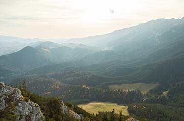 Naklejka premium A breathtaking view unfolds as sunlight filters through mist, illuminating rolling hills and dense forests. Nature's tranquility envelops the expansive valley below