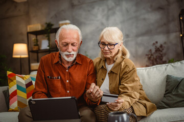 senior husband and wife shop online on tablet with credit card on sofa