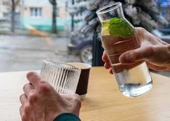 A person is carefully pouring refreshing water infused with mint into a glass while seated at a cafe table during daylight