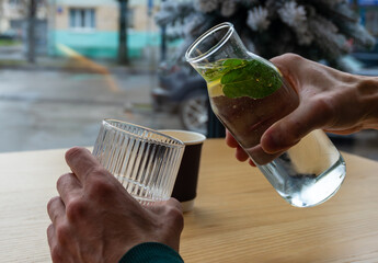 A person pours refreshing water with mint leaves from a carafe into a glass while seated at a cafe...