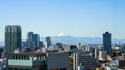 Spectacular view of sacred Mount Fuji from the city of Tokyo, with tokyo city skyline and buildings in the foreground, mt fuji on the horizon line with mountains and clear sky above
