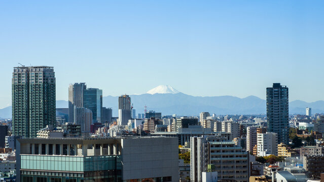 Spectacular view of sacred Mount Fuji from the city of Tokyo, with tokyo city skyline and buildings in the foreground, mt fuji on the horizon line with mountains and clear sky above - Powered by Adobe