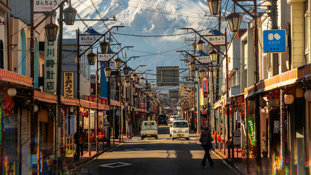 Fujiyoshida, Japan - November 21 2024: Looking up at snow capped mt fuji from the small town with honcho street and traditional japanese buildings and shops. Cool autumn weather with glowing sunlight