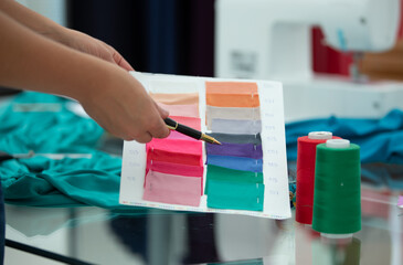 Fototapeta premium A person is holding a pen and looking at a piece of paper with a color chart. The chart has a range of colors, including pink, purple, green, and blue