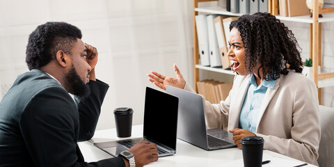 Angry African American woman having fight with her collague at company office, copy space. Millennial black lady shouting at her male coworker, having workplace conflict