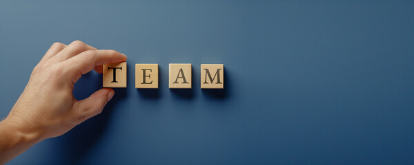 Hand arranging wooden blocks to form the word “TEAM” on a blue background, symbolizing teamwork, collaboration, and the importance of working together to achieve shared goals
