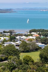 Coastal town with sailboat, houses, and park. Residential area meets the ocean. Sunny day. Devonport, Auckland, Auckland, New Zealand