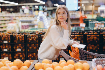 Customer choosing grapefruits in supermarket holding shopping list