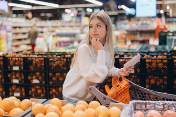 Customer using smartphone and shopping cart in supermarket fruit section