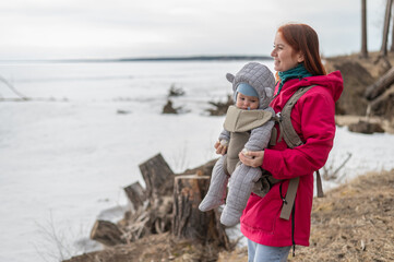 Caucasian red-haired woman walks with her son in an ergo backpack in nature in winter. 