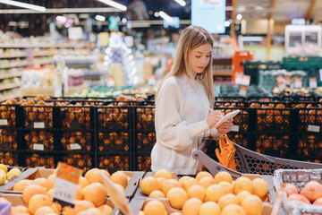 Woman taking notes on shopping list in supermarket fruit and vegetable section