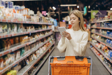 Customer checking shopping list while walking through supermarket aisles