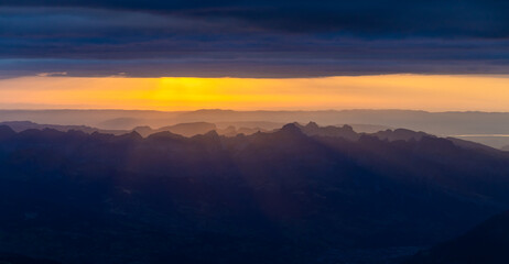 Sunset in the mountains. Red light on the sky with some clouds above the stunning mountain peaks and snow summits of the Alps. Beautiful burning skies horizon at dawn