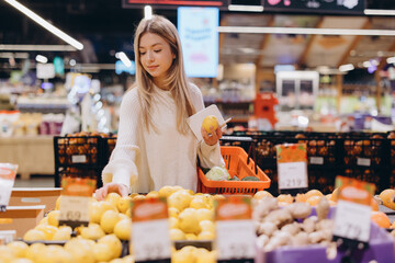 Woman choosing lemons in supermarket holding shopping basket and notepad