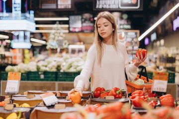 Woman choosing bell peppers in supermarket produce section