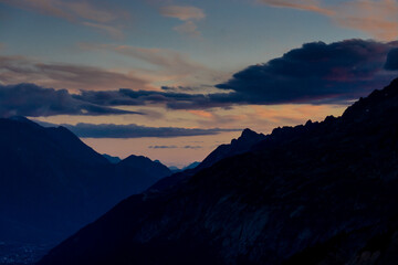 Sunset in the mountains. Red light on the sky with some clouds above the stunning mountain peaks and snow summits of the Alps. Beautiful burning skies horizon at dawn