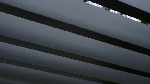 Series of horizontal slats or panels, possibly part of modern architectural structure of louvered roof. Slats are evenly spaced and creating pattern of light and shadow