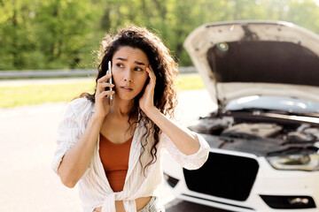 Young woman with smartphone calling towing service on road, having phone conversation with...
