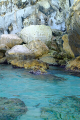 Sharp rocks in a cliff shore formation in turquoise transparent water in Mediterranean beach in Italy