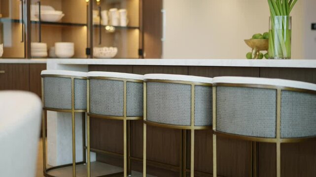 Modern kitchen or dining area with focus on row of stylish bar stools lined up against kitchen island or counter. Contemporary design with combination of light-colored fabric