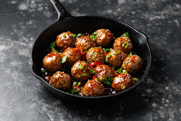 Beef meatballs in teriyaki sauce with sesame seeds, chili and herbs in a cast iron pan