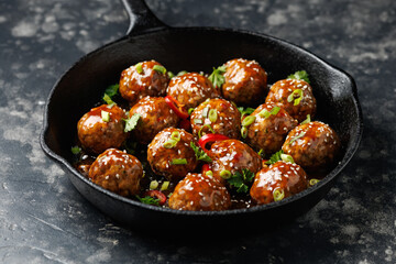 Beef meatballs in teriyaki sauce with sesame seeds, chili and herbs in a cast iron pan
