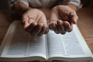 Naklejka premium close up on the hands of an unrecognizable woman reading the bible and praying. Concept of religiosity and mystery