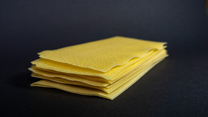 Yellow lasagna sheets are stacked on a black background. Bronze-drawn pasta. Copy space.
