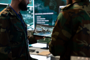 Army IT professional team examining satellite imagery on a tablet, gathering real time battlefield data for a national safety operation. Telecommunications staff work in control room.
