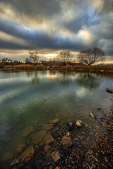 Beautiful landscape with lake and big and smooth clouds in the sky , autumn season, water and trees . Reflections on the water , stormy clouds in the sky . Photography in the forest iwith lake .