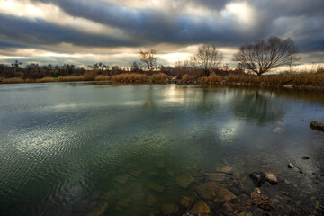 Beautiful landscape with lake and big and smooth clouds in the sky , autumn season, water and trees . Reflections on the water , stormy clouds in the sky . Photography in the forest iwith lake .