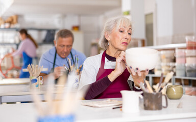 Obraz premium woman covers with white paint almost ready-made jug, which she made herself at pottery workshop