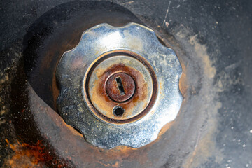 The locked and rusted gas tank cap of an old motorcycle.