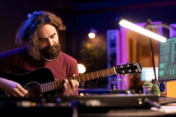Obraz premium Songwriter musician recording sounds on daw software with guitar, enjoying leisure time in home studio office. Audio engineer and producer creating new songs, electronic mixing instruments.