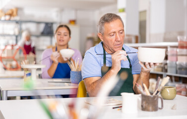 Mature craftsman painting a clay plates acrylic paints in art studio
