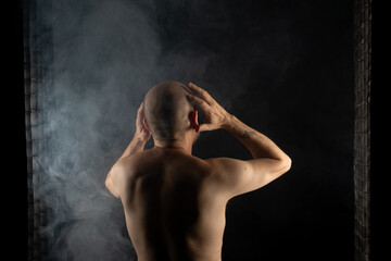 Obraz premium Shirtless, bald man with his back to the camera posing for a photo. Isolated on black background with smoke.