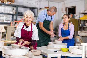 Mature woman learning how to create pottery on potter wheel in a workshop
