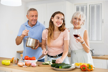 Portrait of smiling mature man, woman and daughter preparing family dinner at kitchen table