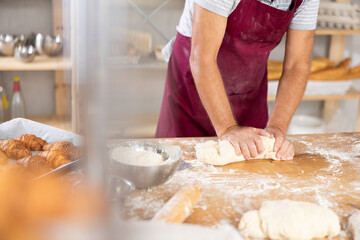 Unrecognizable mature man in vinous apron works in bakery as baker, kneads dough, works with flour with hands close up. Male hand knead dough in bakery