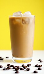 Iced coffee in a tall glass with ice cubes and coffee beans scattered on a white surface against a yellow background.