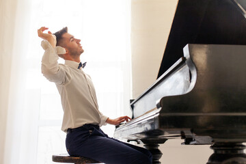 young guy in white shirt plays on old black piano, musician pianist performs melody on acoustic...