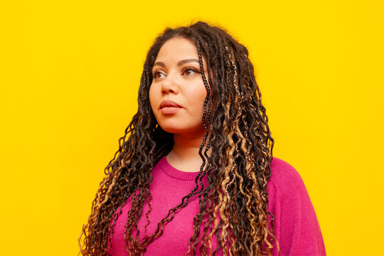 serious plump african american woman with pigtails looking away on yellow isolated background, big plus size girl with dreadlocks