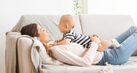 Adorable newborn baby resting on sofa with mother, lying on her chest and smiling, panorama