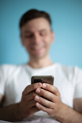 Blurred smiling man in a white t-shirt holding a smartphone, close-up focus on his hands, with a light blue background, creating a modern and relaxed atmosphere for a casual and tech-friendly scene.