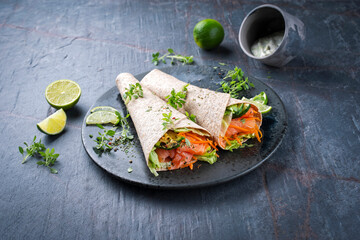 Italian style wrap piada tortilla with cured graved salmon, salad and zucchini served as close-up...