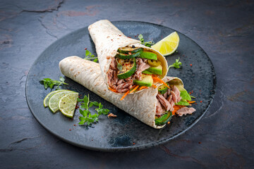 Italian style wrap piada wheat tortilla with tuna fish, vegetable and avocado served as closeup on a Nordic design plate