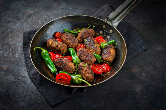 Traditional Croatian cevapi spicy meat ball rolls with tomatoes and paprika served as close-up in a rustic skillet