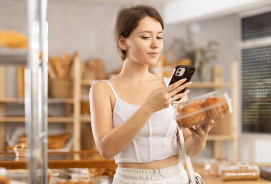 Girl customer holds cake on disposable package and recognizes it using mobile application, learns calorie content of food. Application for determining calorie content of food