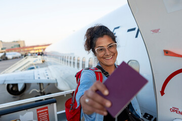 Woman with backpack boarding airplane holding passport and smiling