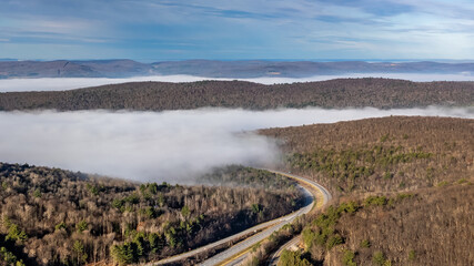 Nearly empty highway on a sunny day descending into thick fog, cloud cover, creating a mysterious...